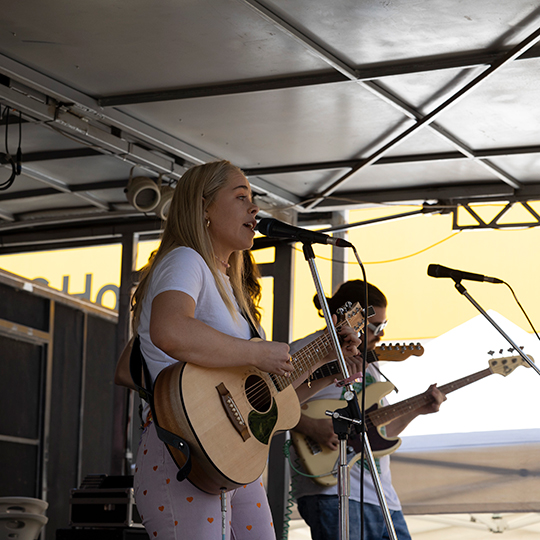 A young woman with blonde hair plays the guitar